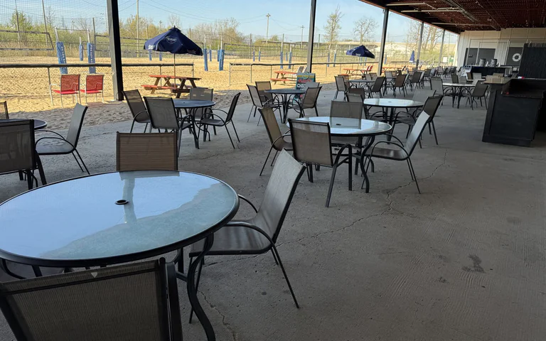Patio tables with volleyball courts in the background at On The Dunes Sports